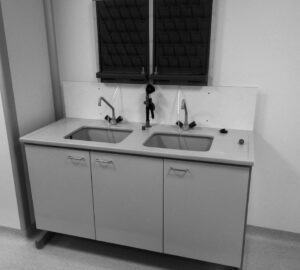 Na zdjęciu przedstawiono laboratoryjny stół zlewowy który posiada dwie komory zlewowe, blat z żywicy, oczomyjkę awaryjną i dwa ociekacze kołkowe