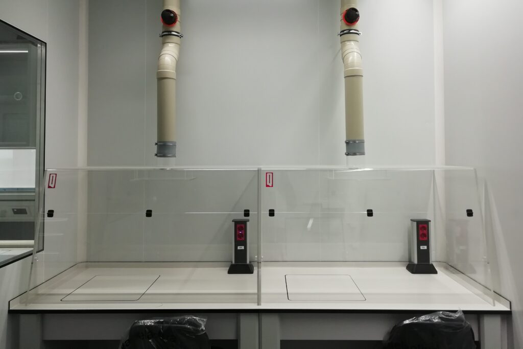 Na zdjęciu przedstawione dwa wyciągi chemiczne z przezroczystego PMMA. Wyciągi postawione są na stołach laboratoryjnych i podłączone do wentylacji